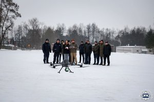Nowoczesny dron ze skanerem 3D w powietrzu, na drugim planie widać grupę ludzi, w tym operatora drona i policjantów.