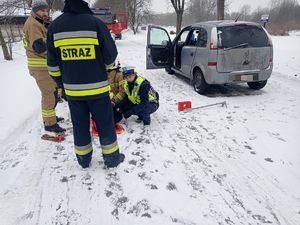 Policjanci i strażacy przy potrzebującym pomocy mężczyźnie. Z boku widać zaparkowanego Opla a z tyłu wóz strażacki.