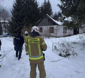 Dwaj strażacy i policjant przy budynku, w którym zawalił się dach.