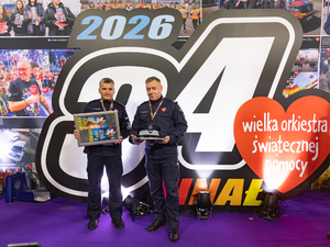 Zastępca komendanta głównego Policji z policjantem prezentują czapkę generalską i vouchery.