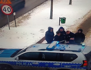Stopklatka z nagrania monitoringu przedstawia policjantów przy radiowozie z mężczyzną, któremu udzielili pomocy.