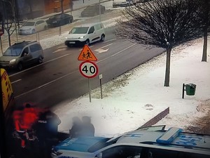 Stopklatka z nagrania monitoringu przedstawia ratowników medycznych i policjantów przy karetce pogotowia.