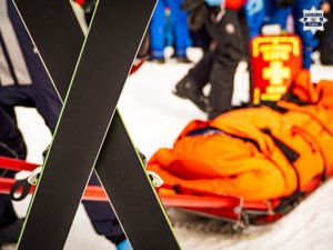 Skrzyżowane narty, śnieg, zima, w tle nosze ratownicze.