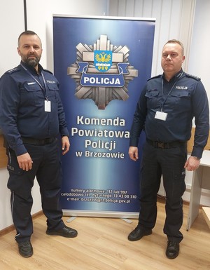 Dwaj umundurowani policjanci pozują do zdjęcia.