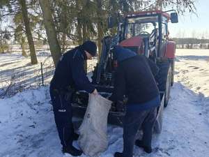 Mężczyzna ładuje drewno do worka, który trzyma policjant.