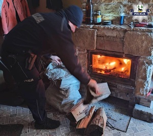 Policjant wrzuca drewno do pieca.