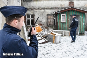 Dwaj policjanci stoją przed opuszczonym budynkiem.