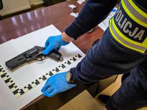 Policjant i zabezpieczona broń leżąca na stole.
