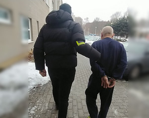 Nieumundurowany policjant prowadzi zatrzymanego.