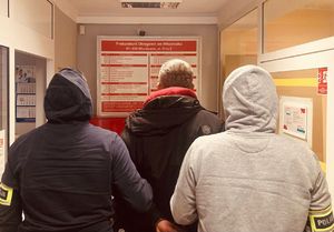 Dwaj funkcjonariusze z zatrzymanym na korytarzu w budynku prokuratury.