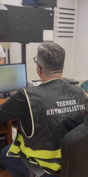 plecy policjantka, który siedzi przy biurku. na plecach ma napis technik policyjny.