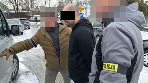 Dwaj policjanci z zatrzymanym mężczyzną przy nieoznakowanym radiowozie.