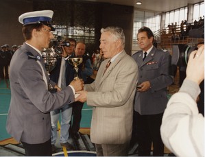 elegancko ubrany mężczyzna wręcza odznakę policjantowi, w tle stoi świętej pamięci komendant główny policji.