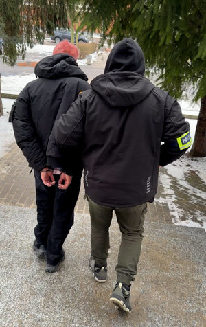 Funkcjonariusz prowadzi zatrzymanego męzczynę.