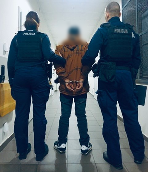 dwoje policjantów prowadzi zatrzymanego przez korytarz.