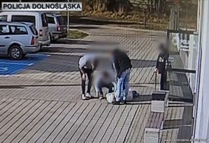 Stopklatka z nagrania monitoringu. Policjanci udzielają pomocy kobiecie leżącej przed budynkiem.