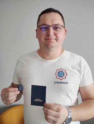 Nieumundurowany policjant, który oddał szpik, trzyma w dłoni odznakę i legitymacje dawcy przeszczepu.