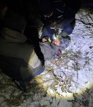 Odnaleziona osoba leży na ziemi, obok dwaj funkcjonariusze.