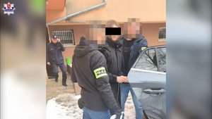 Mężczyzna w kajdankach, prowadzony przez policjantów.