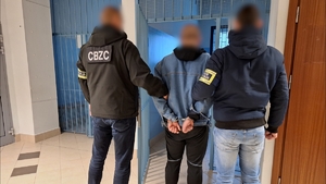 Dwaj policjanci CBZC prowadzą zatrzymanego do okratowanego pomieszczenia.