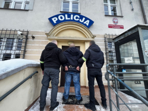 dwóch policjantów stoi z zatrzymanym przed budynkiem policji.