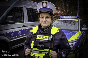 Policjantka stoi przed dwoma radiowozami.