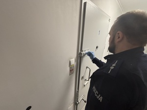 Funkcjonariusz zamyka metalowe drzwi pomieszczenia dla zatrzymanych przesuwając zasuwę.