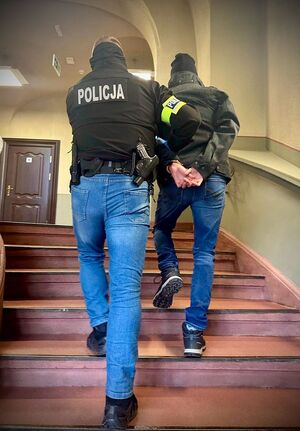 Funkcjonariusz prowadzi zatrzymanego mężczyznę zakutego w kajdanki.