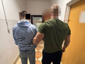 Funkcjonariusz trzyma zatrzymanego zakutego w kajdanki.