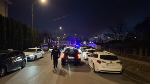 Policjant idzie ulicą w kierunku stojącej taksówki. Po obu stronach ulicy stoją zaparkowane samochody osobowe, w tym inne taksówki.