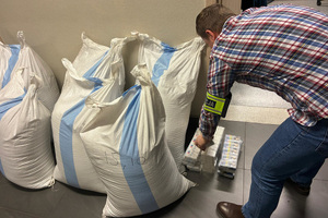 Policjant kładzie na podłodze sztangi zabezpieczonych papierosów, obok w workach stoi zabezpieczona nielegalna krajanka tytoniowa.