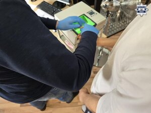 Policjanci prowadzą zatrzymanego. Pobierają odciski palców. pieniądze rozłożone na stole.