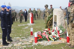 Grupa żołnierzy i policjanci składający hołd przy pamiątkowej tablicy.