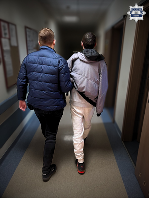 Policjant prowadzi korytarzem zatrzymanego.