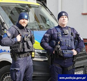 dwóch policjantów stoi przed radiowozem.