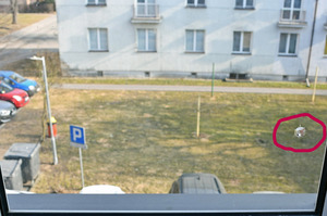 Ślad w szybie po kuli. W tle trawnik przed blokiem mieszkalnym.