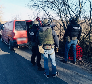 Policjanci stoją przy samochodzie. Podejrzany leży na ziemi.