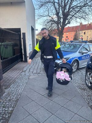 policjant niesie nosidełko z małym dzieckiem.