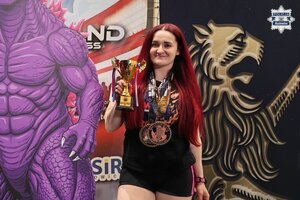 Sportsmenka trzyma w dłoni puchar i ma na szyi zawieszone trzy medale.