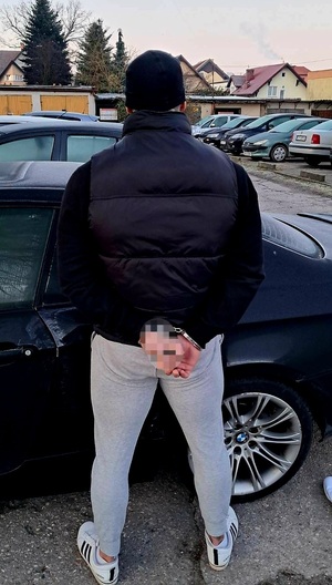 Policjanci prowadzą zatrzymanego. Mężczyzna w kajdankach.