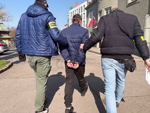 dwóch policjantów prowadzi zatrzymanego.