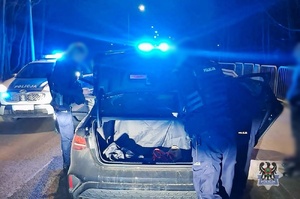 Noc. policjanci podczas kontroli drogowej przeszukują bagażnik. Żółte paczki.