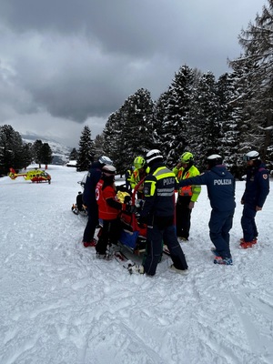 policjanci stoją obok proszkowanego, któremu włoscy ratownicy udzielają pomocy.
