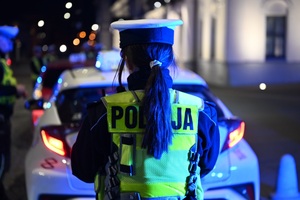 plecy policjantki. przed nią stoi biała taksówka.