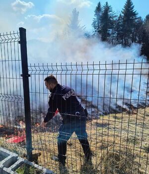 Policjanci gaszą płonącą łąkę.