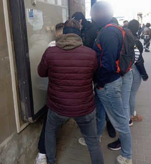 Policjanci prowadzą zatrzymanego,. Mężczyzna ma skute kajdankami ręce.