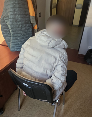 Policjanci prowadzą zatrzymanego,. Mężczyzna ma skute kajdankami ręce.