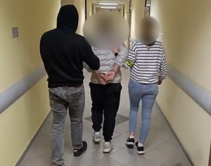 Policjanci prowadzą zatrzymanego,. Mężczyzna ma skute kajdankami ręce.