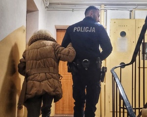 policjant prowadzi po schodach seniorkę.