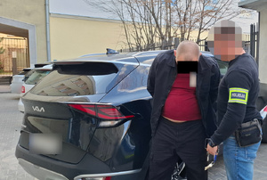 Policjant z zatrzymanym mężczyzną przy radiowozie nieoznakowanym.